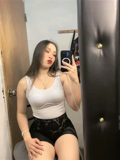A woman taking a mirror selfie in a white top and black shorts