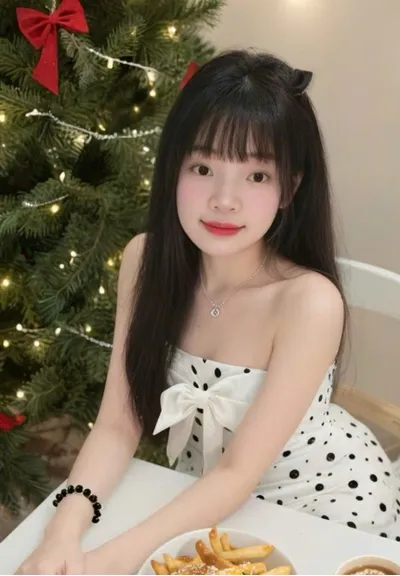 A woman in a polka dot dress sitting by a decorated Christmas tree