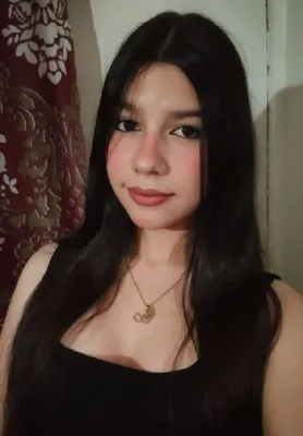 A young woman with long black hair in a black top taking an indoor selfie