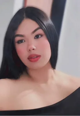 A woman with shoulder-length dark hair in a black off-shoulder top taking a selfie